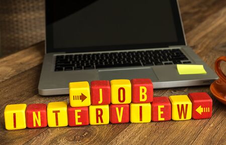 Job Interview written on a wooden cube in front of a laptopの写真素材