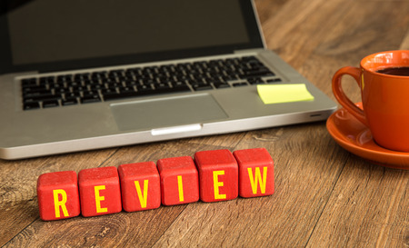 Review written on a wooden cube in front of a laptopの写真素材
