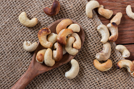 Tasty cashew nuts in wooden spoon on wooden table. Space for text. Top view