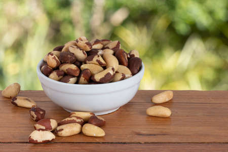 Brazilian nut, known as "Castanha do ParÃ¡" in a bowl on a wooden table with an unfocused garden backgroundの写真素材