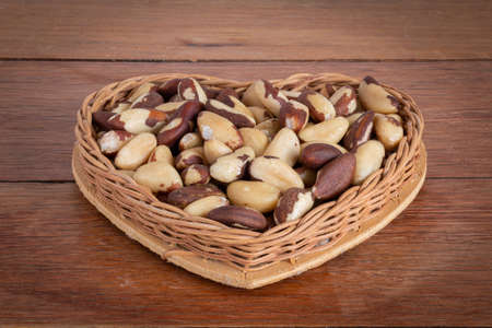 Brazilian nut, known as "Castanha do ParÃ¡" in a heart-shaped basket on a wooden tableの写真素材