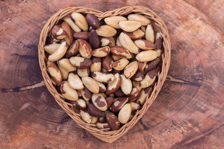 Brazilian nut, known as Castanha do ParÃ¡ in a heart-shaped basket on a wooden table. Top view....