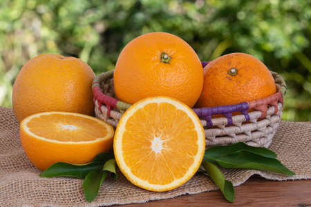 Ripe whole oranges and cut pieces in basket on wooden table with blurred green background. Copy spaceの写真素材