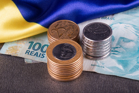 One hundred reais notes and coins over Brazilian flag.