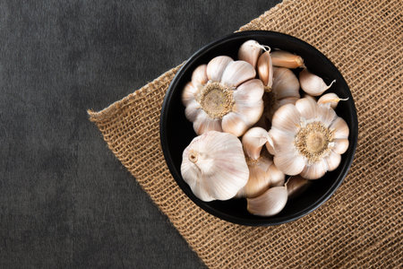 Garlic Cloves and Bulb in black bowl on jute and dark background.