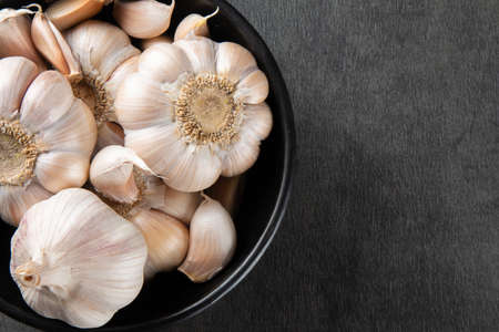Garlic Cloves and Bulb in Black Bowl with Dark Background.の写真素材