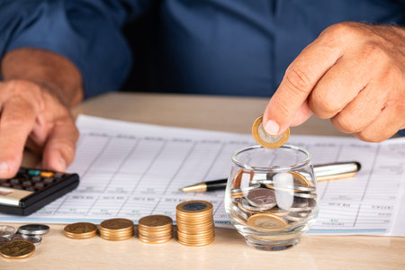 Businessman holding coins and putting into glass pot. Saving concept for financial accounting.の写真素材