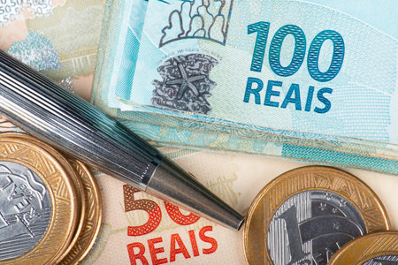 Close-up shot of Brazilian Real banknotes and coins with a pen, illustrating finance, economy, or business concepts in Brazil.の写真素材