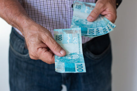 A man holding and giving Brazilian 100 real banknotes representing money finance and payment.