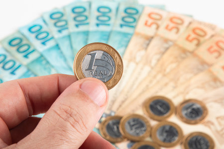 Person holding Brazilian Real coin with banknotes in background. Brazilian money concept.の写真素材