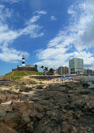 Barra Lighthouse with beach rocks and city buildings in Salvador Bahia Brazil.の写真素材
