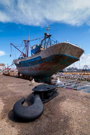 A fishing boat docked at the Essaouira port waits for a full repair with a boat hook in the foregroundの写真素材