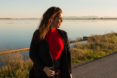 Beautiful brunette woman portrait standing outside in a sunny day, with a lake in background.の写真素材