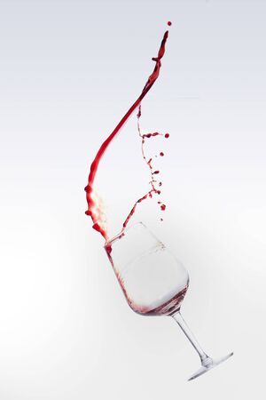Red wine splashing out of a glass, isolated over white backgroundの写真素材