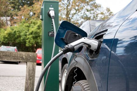 Electric Car in Charging Station with the power cable supply plugged in with the blurred background. Eco-friendly alternative energy concept.の写真素材