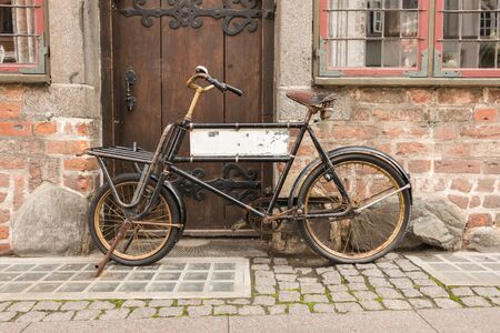 An old bicycle, in front of a brick wall and an old wooden door. The bicycle has a blank sign inside the frame.  Old conceptの写真素材