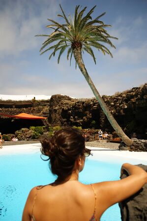 A woman on her back slightly unfocused facing an idyllic landscape with a palm tree over a design  pool in Jameos del Agua in Lanzarote (Spain)の写真素材