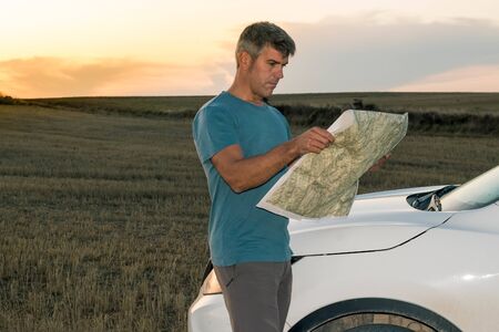 A lost man in the middle of the field with his car consults a map at sunset. Lifestyle conceptの写真素材