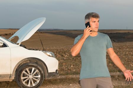 A worried man in the middle of the field calling the insurance of his broken down car for assistance at sunset. Lifestyle conceptの写真素材