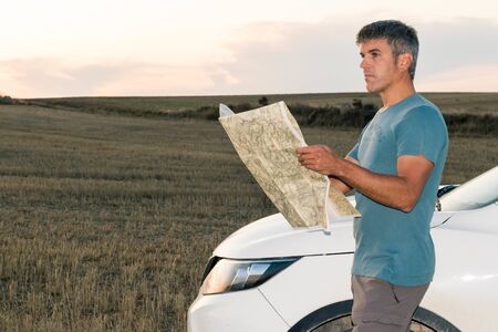 A lost man in the middle of the field with his car consults a map at sunset. Lifestyle conceptの写真素材