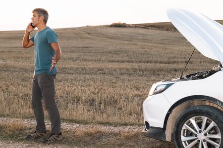 An angry man in the middle of the field calling the insurance of his broken down car for assistance at sunset. Lifestyle conceptの写真素材