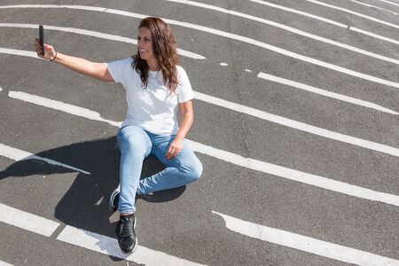 Young woman makes a selfie sitting on the grey floor with white lines.の写真素材