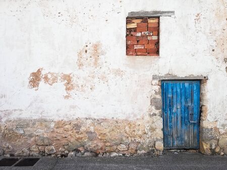 Worn facade of an old house with a blue wooden door and a bricked window in a rural village in Spain. Architectureの写真素材