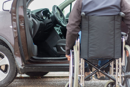 A man in a wheelchair trying to get into the driver's seat of a car. Accessibility concept