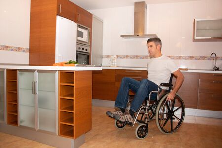 A man in a wheelchair moves through the kitchen. Disability conceptの写真素材