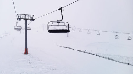 Chairlift moving in foggy and snowy day. Snow covered the hills surrounding. Ski resort