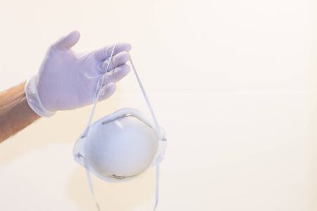 A hand with a protective glove holds a medical mask on a white background. Pandemic conceptの写真素材