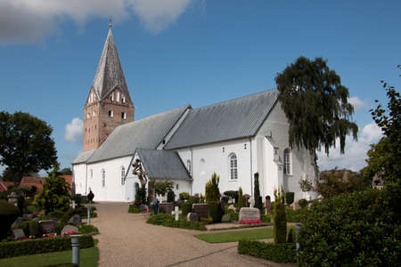Tonder, Denmark - August 20, 2019: Mogeltonder church with white walls and a big bell tower and a cemetery around it in a small town in Denmark. Catholicism conceptのeditorial素材