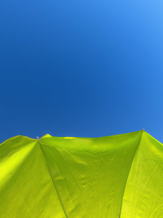 Vertical background image of a yellow beach umbrella with blue sky in the background. Summery...