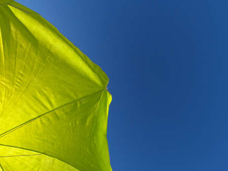 Background image of a yellow beach umbrella with blue sky in the background. Summery conceptの写真素材