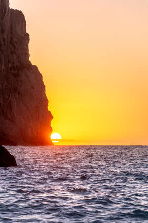The sun setting behind a cliff above the horizon line of the sea with a golden sky. Vacations conceptの写真素材