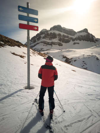 Skier in front of a ski resort signpost doubting which ski slope to go to. Skiing conceptの写真素材