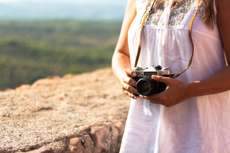 Young woman holds an old camera hanging from her neck next to a stone wall. Photography concept