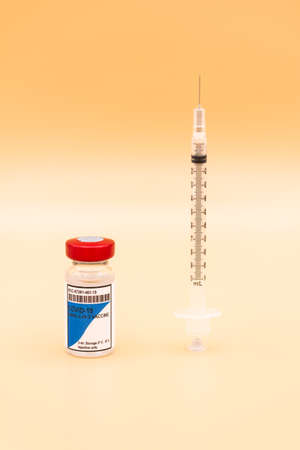 A vial of the COVID-19 vaccine with a syringe placed upright next to it on an orange background. Coronavirus conceptの写真素材