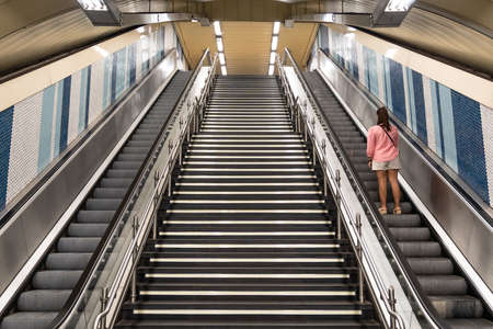 View of escalators with a staircase in the center in the subway and a woman on her back going up one of the escalators. Transport conceptの写真素材