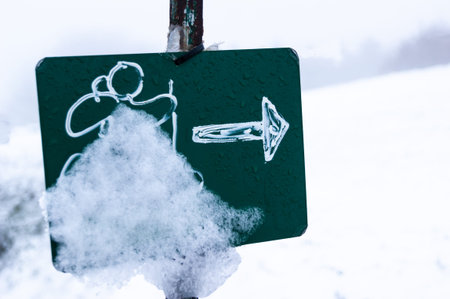 Close-up of a green sign indicating a trail, covered in snow. Hiking concept