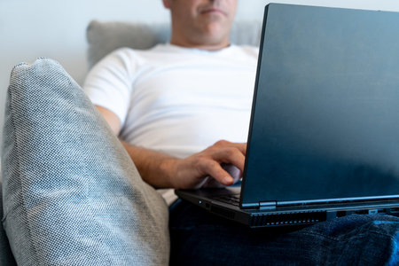 Foreground on unrecognizable man sitting in an armchair using a laptop. Focus on the laptop