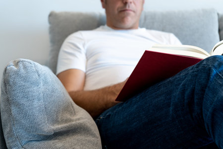 Unrecognizable man sitting in an armchair reading a book. Focus on the book