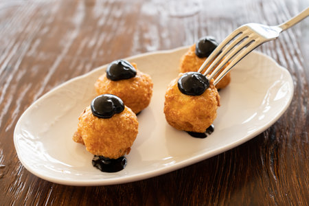 Close-up of a fork poking a squid ink croquette from a gourmet dish. Spanish cuisine conceptの写真素材