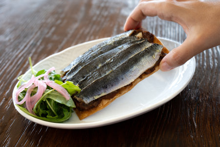 Close-up of a woman's hand taking a gourmet-style sardine toast from the plate. Spanish cuisine conceptの写真素材