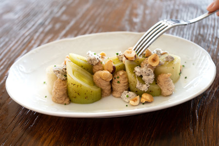 Close-up of a fork poking into a plate of leek salad with meuniere sauce, gourmet style. Spanish cuisine conceptの写真素材