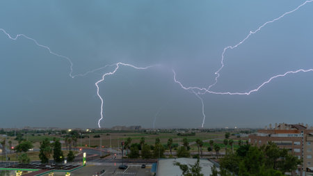 Stormy sky with several huge lightning bolts striking the ground on the outskirts of a city over agricultural fields. weather conceptの写真素材