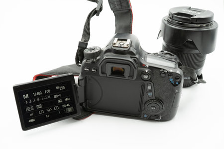 Valencia, Spain - August 8, 2021: Canon model 70D DSLR camera seen from behind with its digital display flipped down showing the menu and a Canon lens in background on a white background. Product photographyのeditorial素材