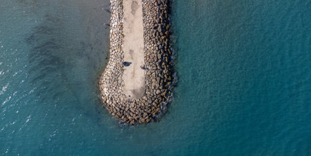 Aerial view of a breakwater stretching into the sea. Tranquility of ocean waves meeting the structure. Ideal for backgrounds or travel concepts. Copy space. Space for textの写真素材