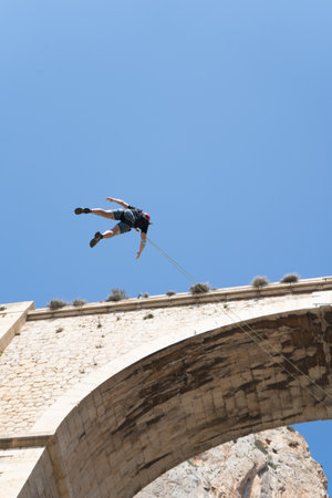 View from below of an unrecognizable person after bungee jumping from an anti stone bridge. Adventure sports concept. Extreme emotionsの写真素材