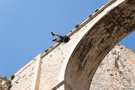 Bottom view of an unrecognizable person bungee jumping from a historic stone bridge. Adventure sports concept. Mascarat bridgesの写真素材